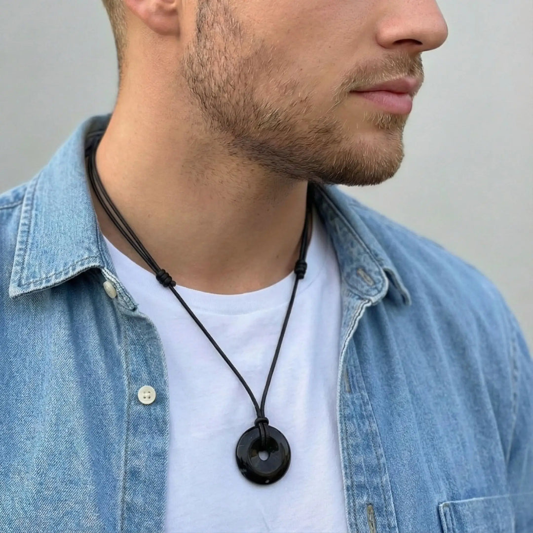 Man wearing a black tourmaline necklace with a round pendant, dressed in a denim jacket and white shirt.