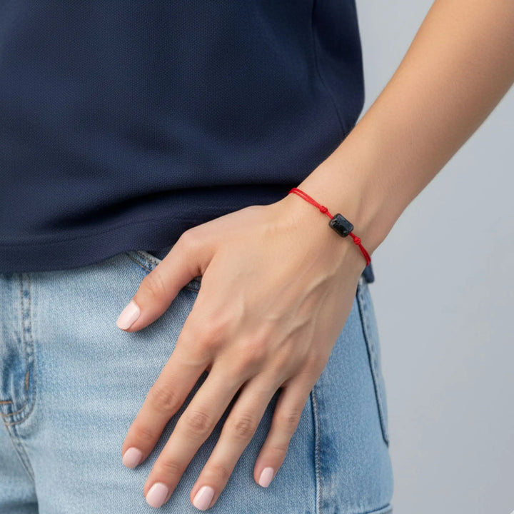 Person wearing a black tourmaline red bracelet on a plain background