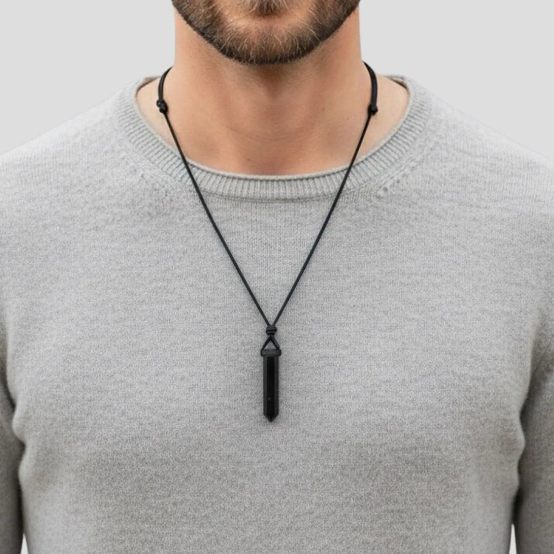 Man wearing a gray sweater with a black tourmaline pendant necklace against a light gray background