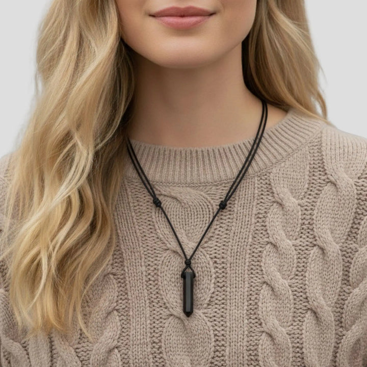 Person wearing a black tourmaline  point necklace with a pendant against a neutral background