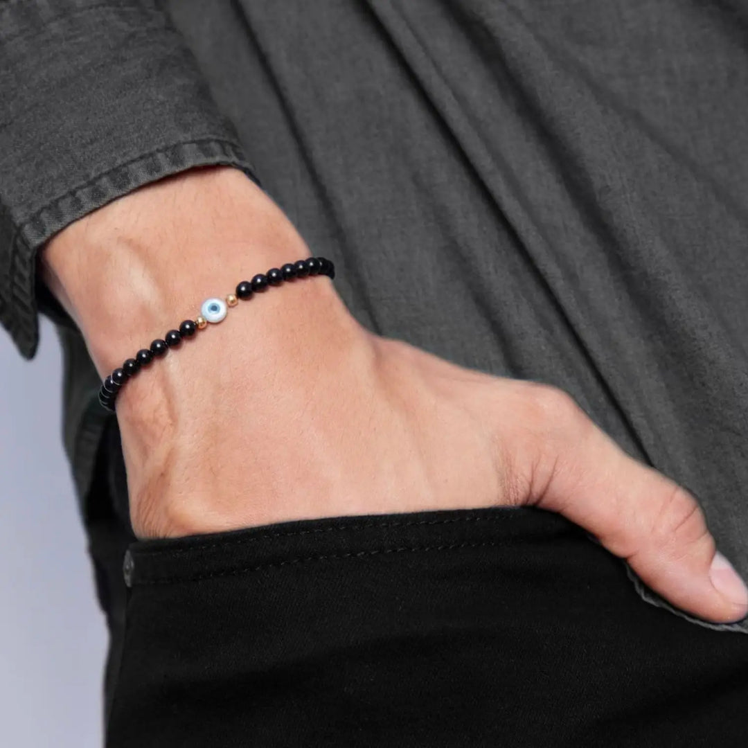 14K Gold and Black Tourmaline bracelet with Mother of Pearl evil eye on a wrist, highlighting the gold accents and snug fit - Luck Strings