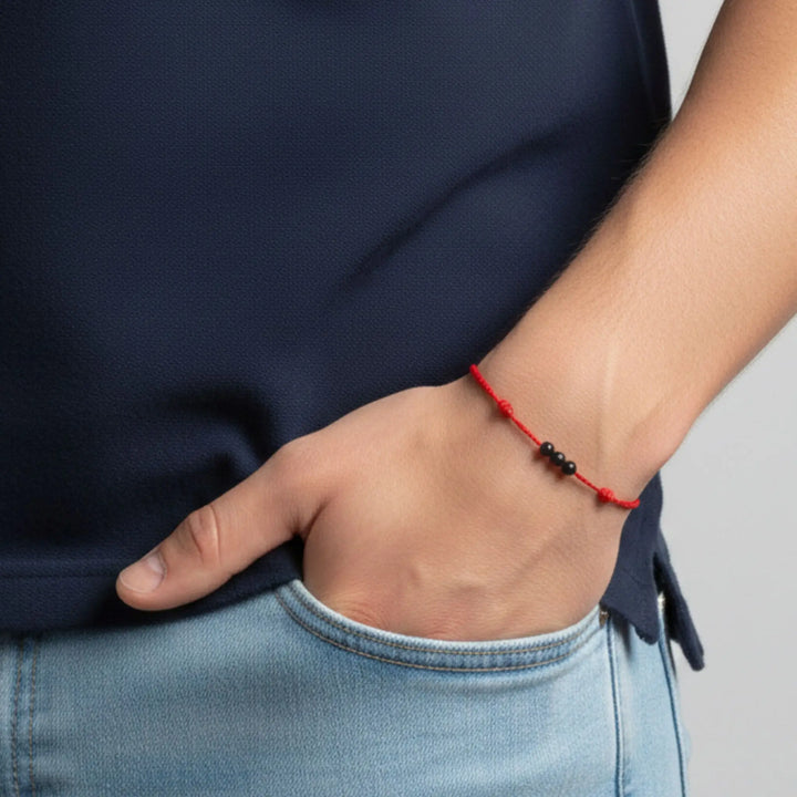 Hand in pocket wearing triple black tourmaline round bead bracelet on red nylon cord.