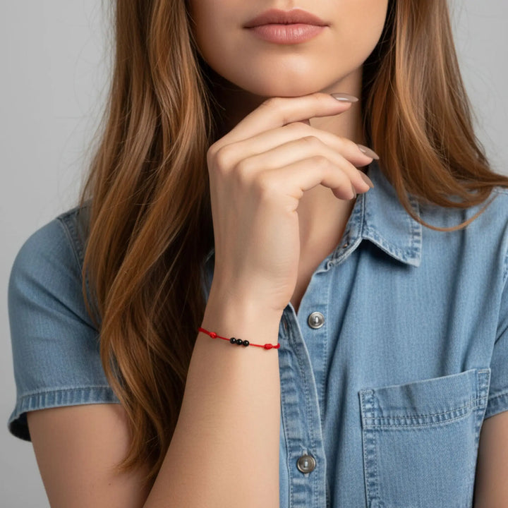 Woman wearing triple black tourmaline round bead bracelet on red nylon cord.