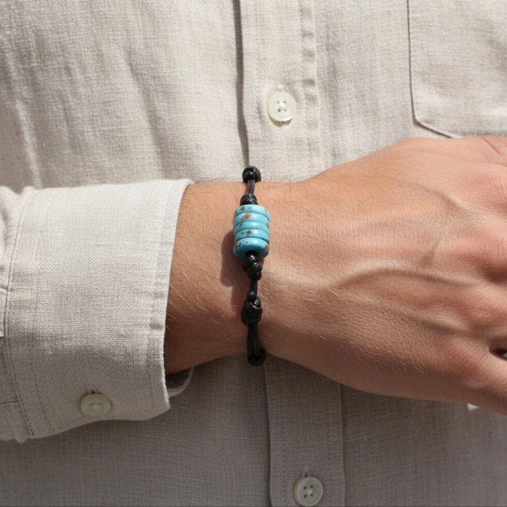 Man wearing adjustable turquoise bone bead bracelet on black cord, wrist detail.
