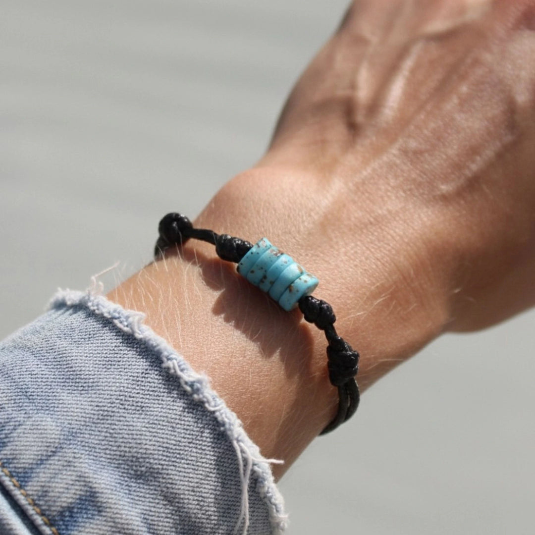 Close-up of adjustable turquoise bone bead bracelet on black cord.
