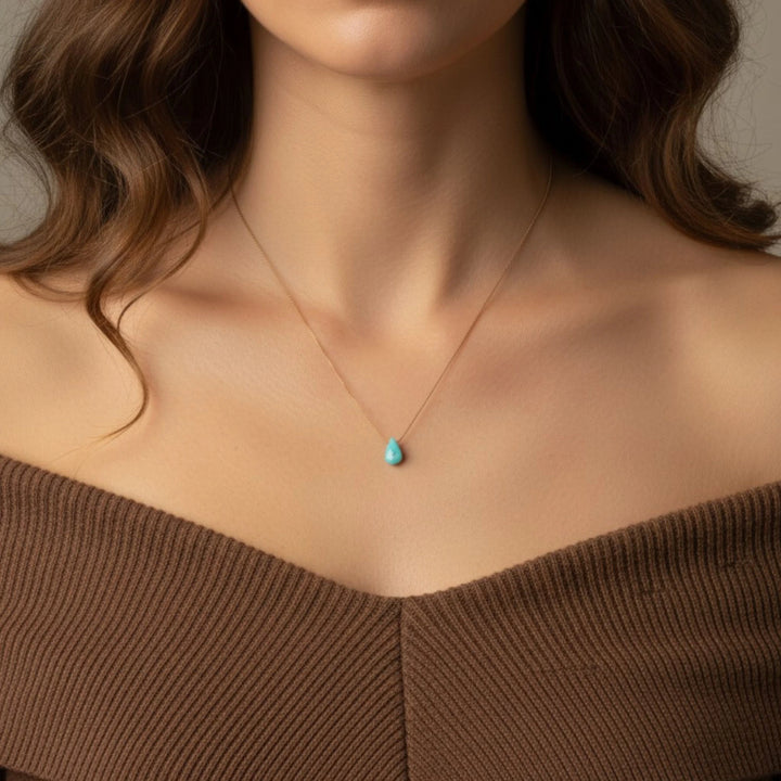 Necklace with a turquoise pendant worn by a person in a brown top