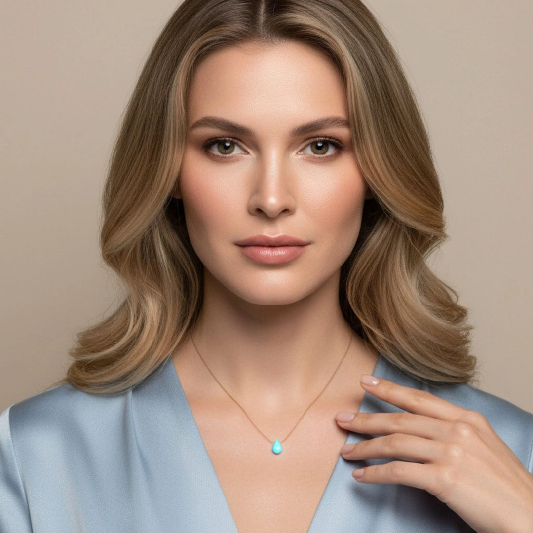 Woman wearing a light blue top with a necklace featuring a turquoise pendant against a beige background