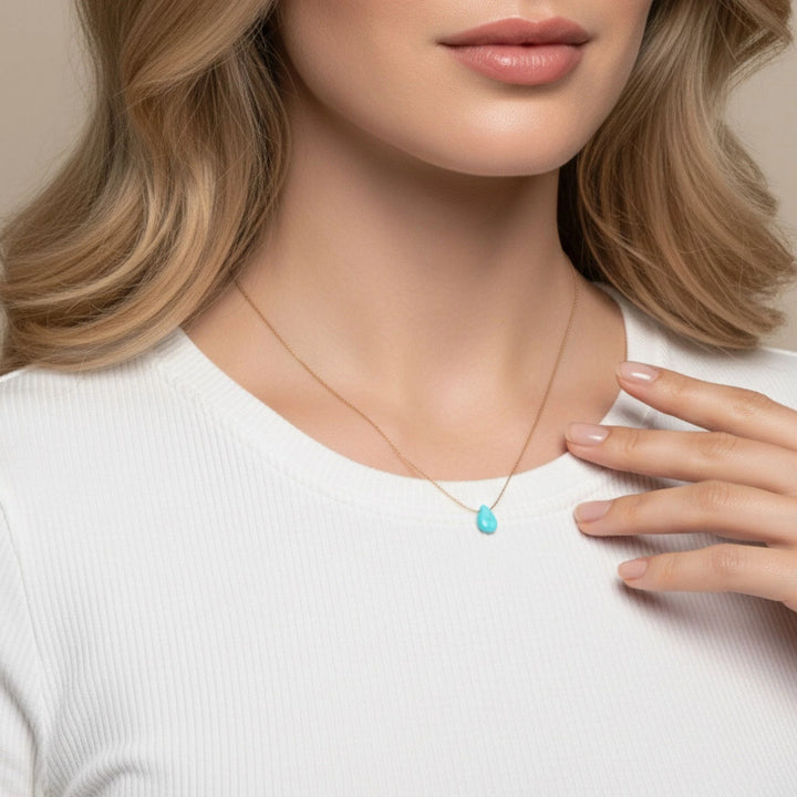 Woman wearing a necklace with a turquoise pendant on a neutral background