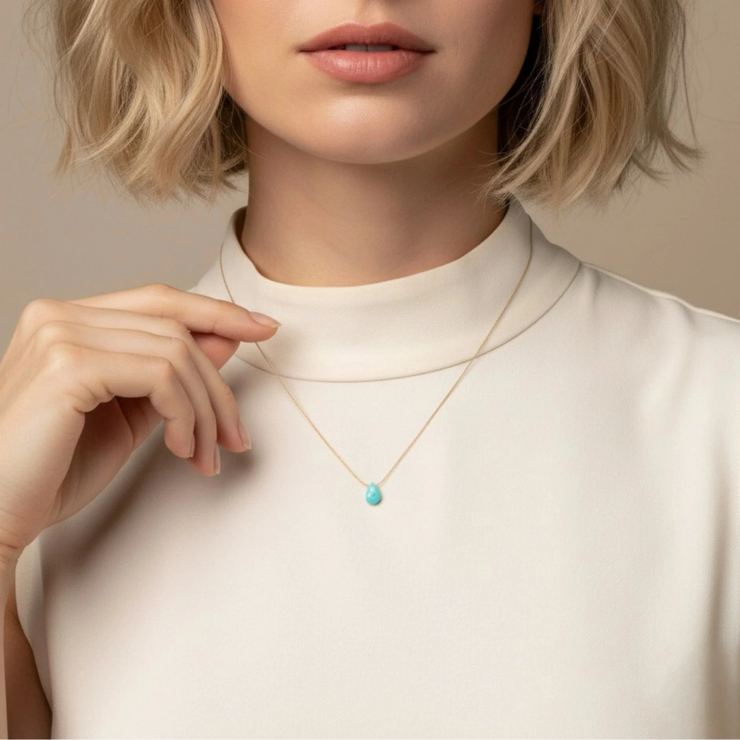 Woman wearing a necklace with a turquoise pendant against a neutral background
