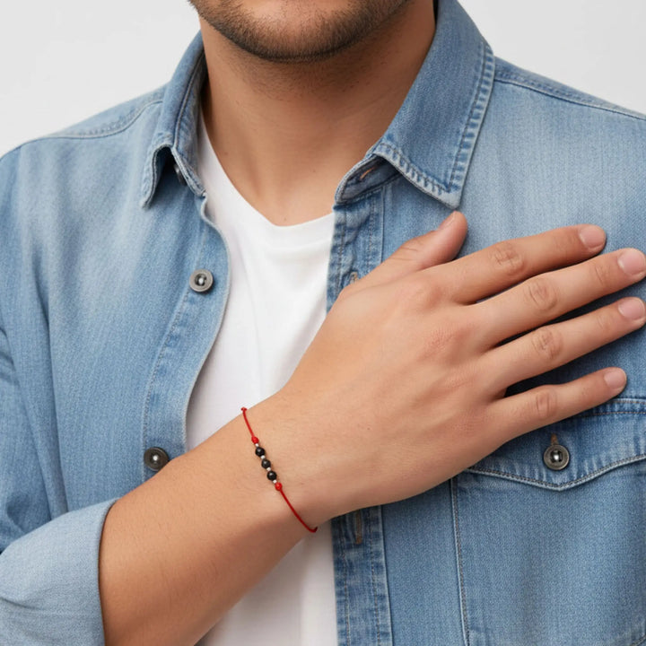 Person wearing a blue denim jacket with a hand on their chest, wearing a red bracelet.