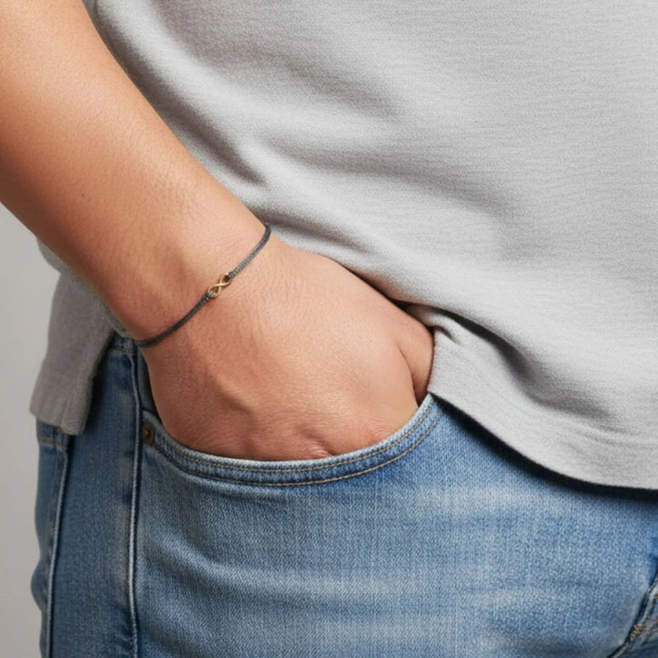 Person wearing a gray shirt and blue jeans with a infinity bracelet on a neutral background