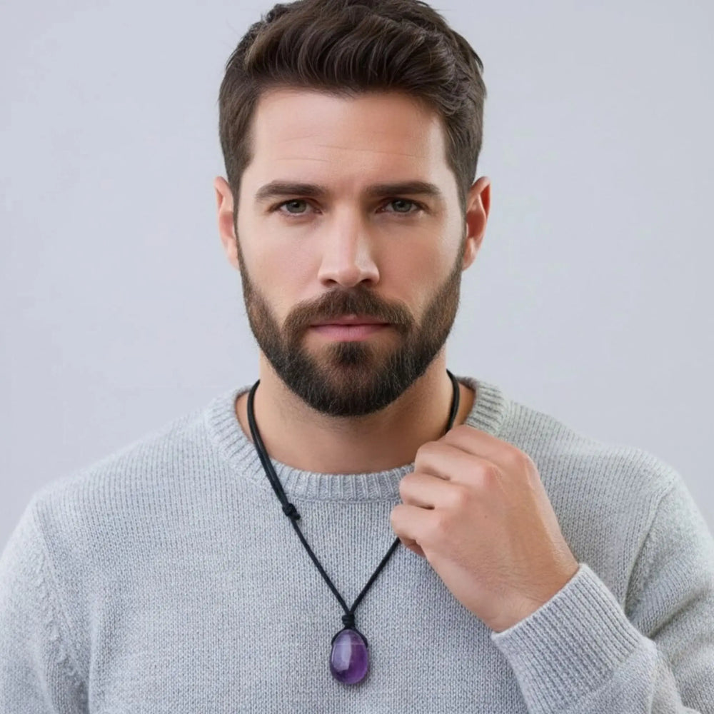 Man wearing a gray sweater with a necklace featuring a purple amethyst  pendant against a light gray background