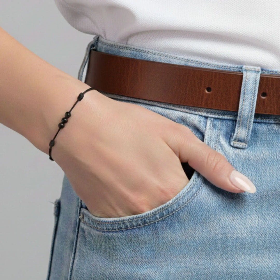 Person wearing a black tourmaline bracelet and a brown belt and blue jeans with a neutral background