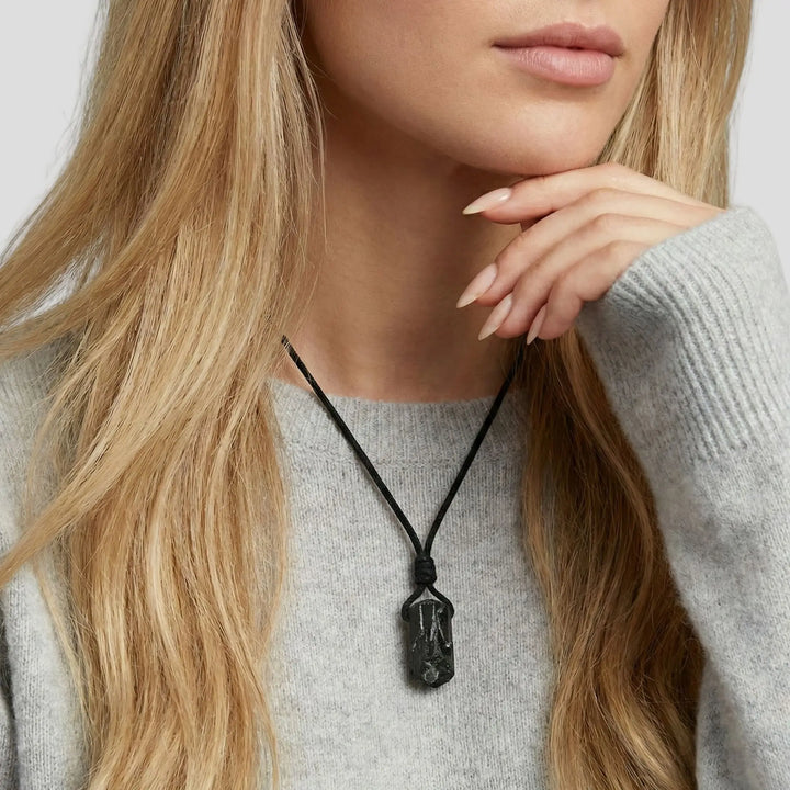 Person wearing a necklace with a pendant, set against a neutral background