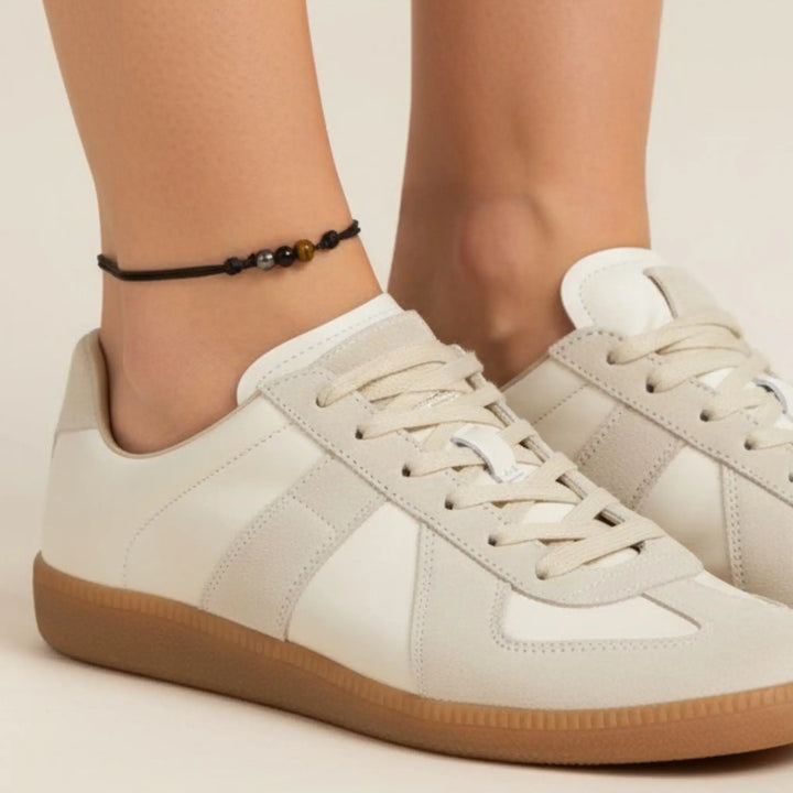 Beige sneakers worn with a red anklet on a neutral background