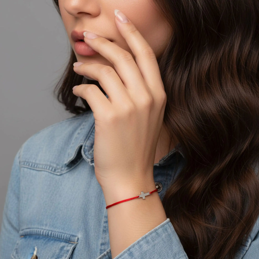 Woman wearing a red bracelet with a small cross  on a gray background