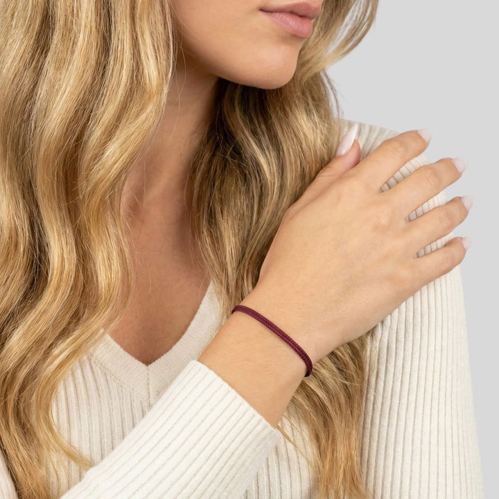 Woman wearing a burgundy bracelet on a light gray background