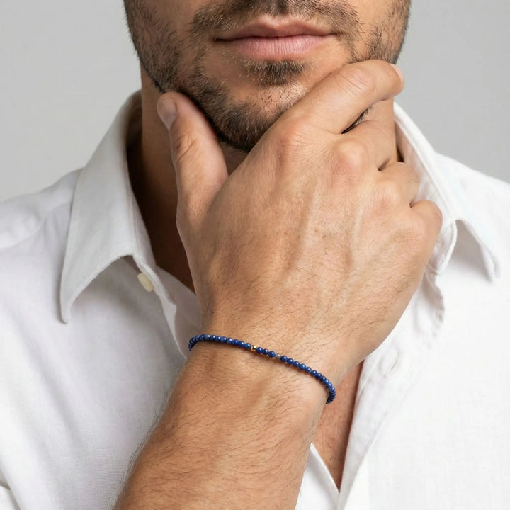 Man wearing a blue lapis lazuli beaded bracelet on his wrist, with a plain background