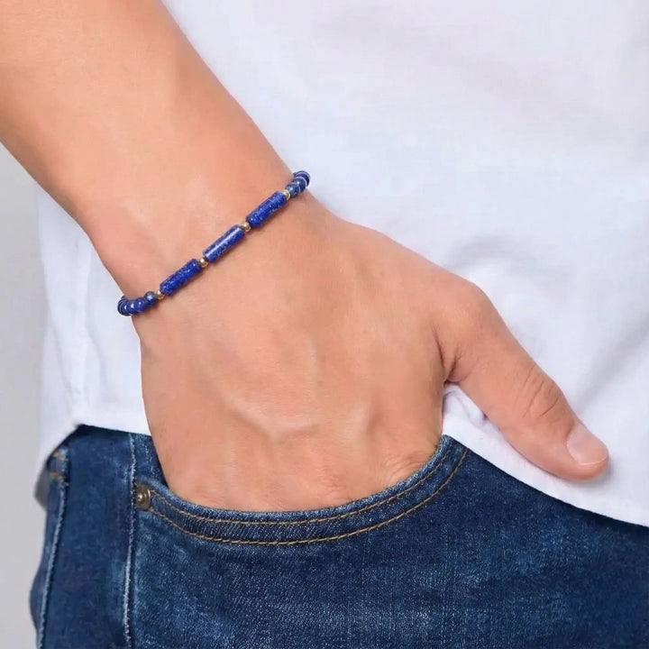 Person wearing a blue beaded bracelet on a plain background