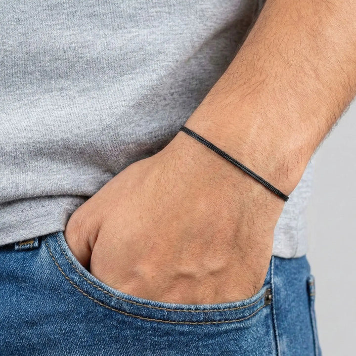 Person wearing a black bracelet on wrist with gray shirt and blue jeans