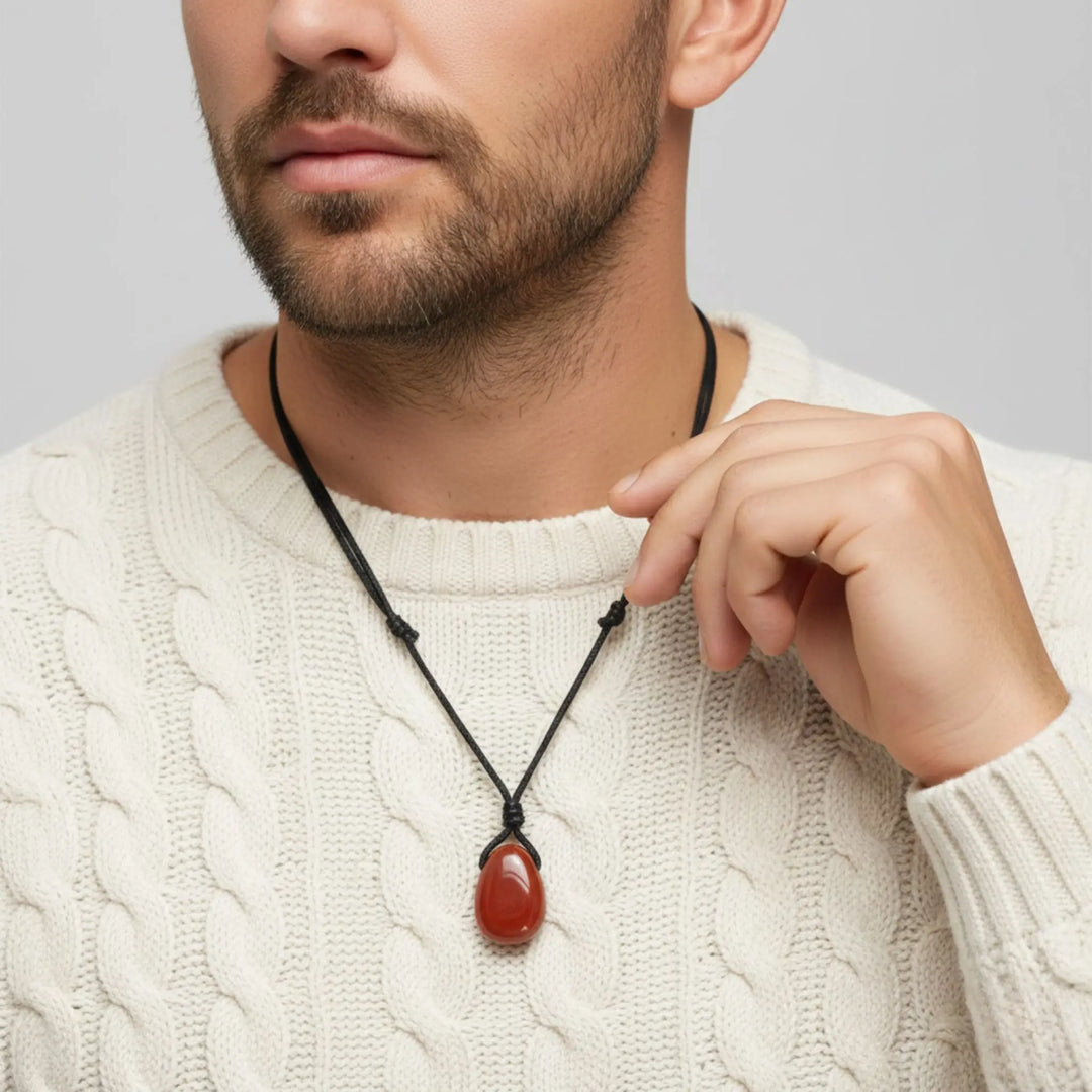 Man wearing a necklace with a red jasper pendant against a neutral background