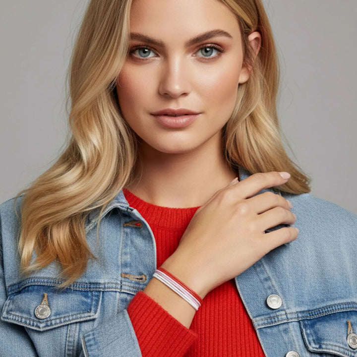 Woman wearing a denim jacket over a red sweater, featuring a red, pink, and white bracelet trio against a neutral background