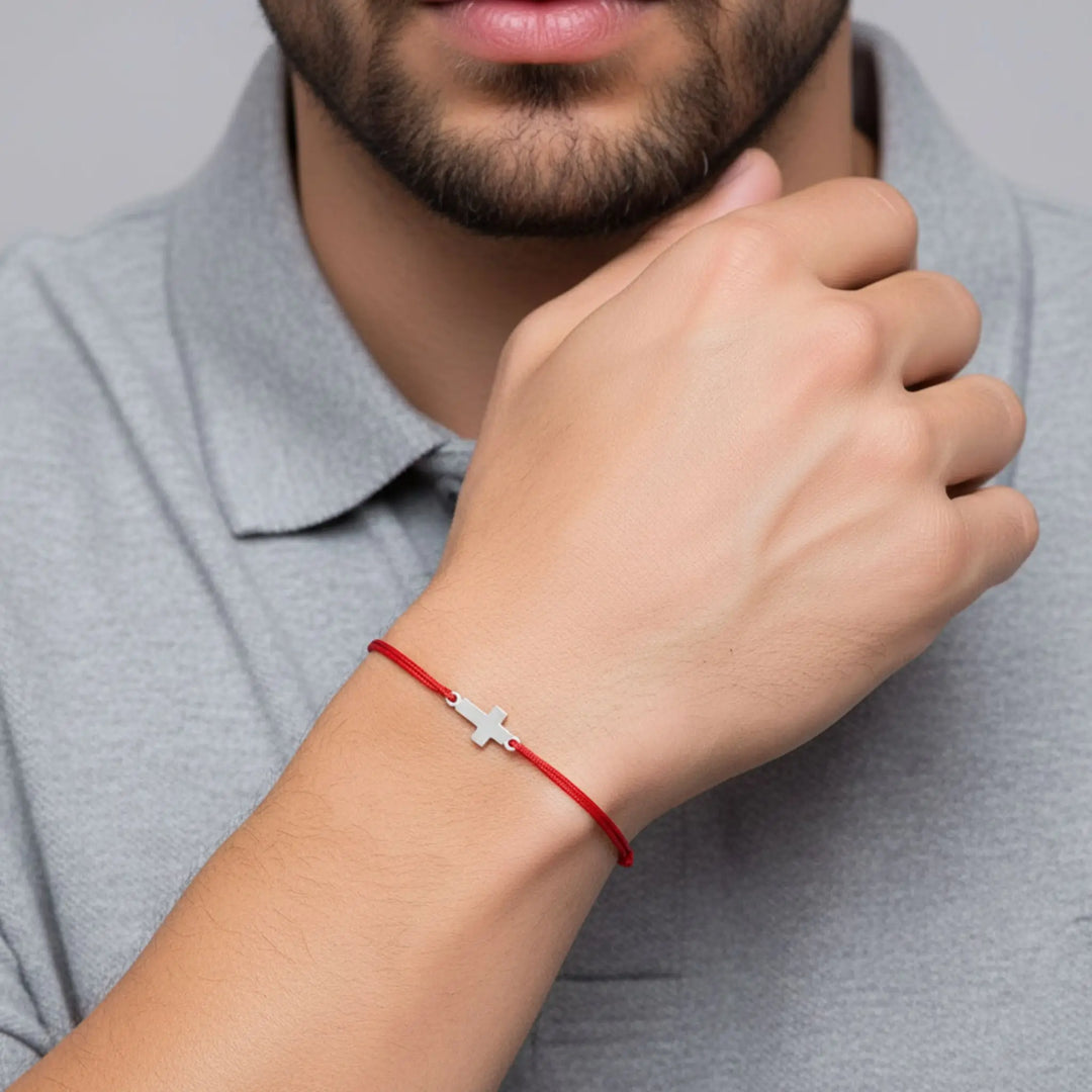 Person wearing a red bracelet with a silver cross charm on a neutral background