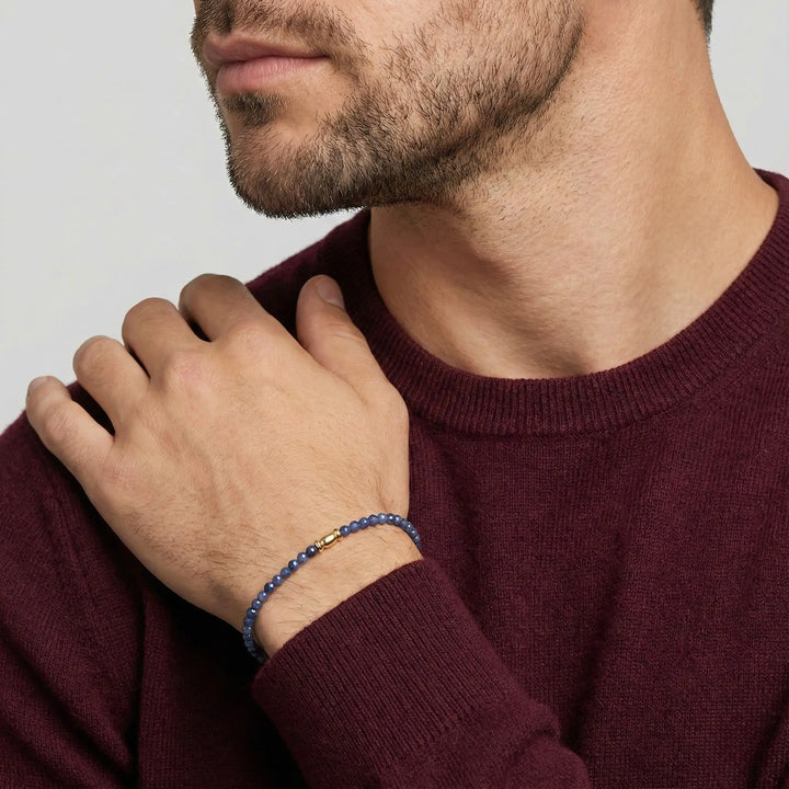 Man wearing a maroon sweater with a close-up of his hand and sapphire bracelet on a light gray background