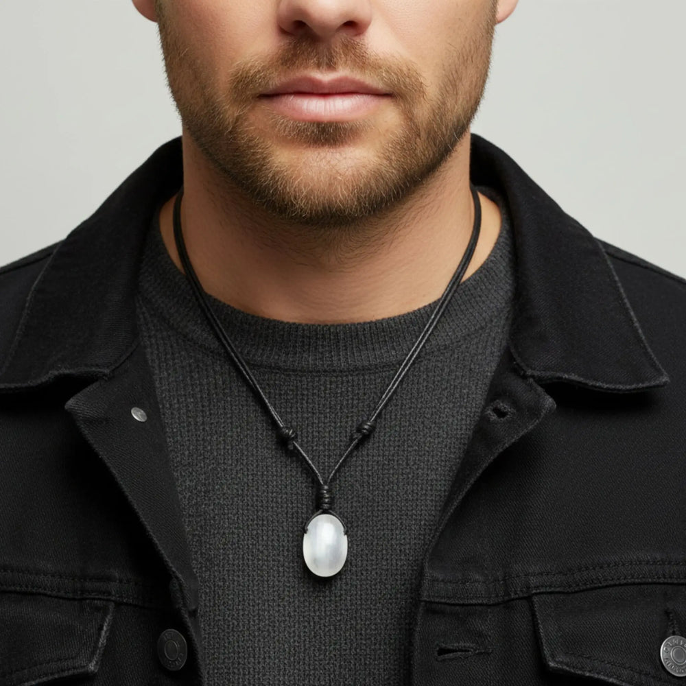 Man wearing a black jacket and necklace with a white selenite pendant on a neutral background