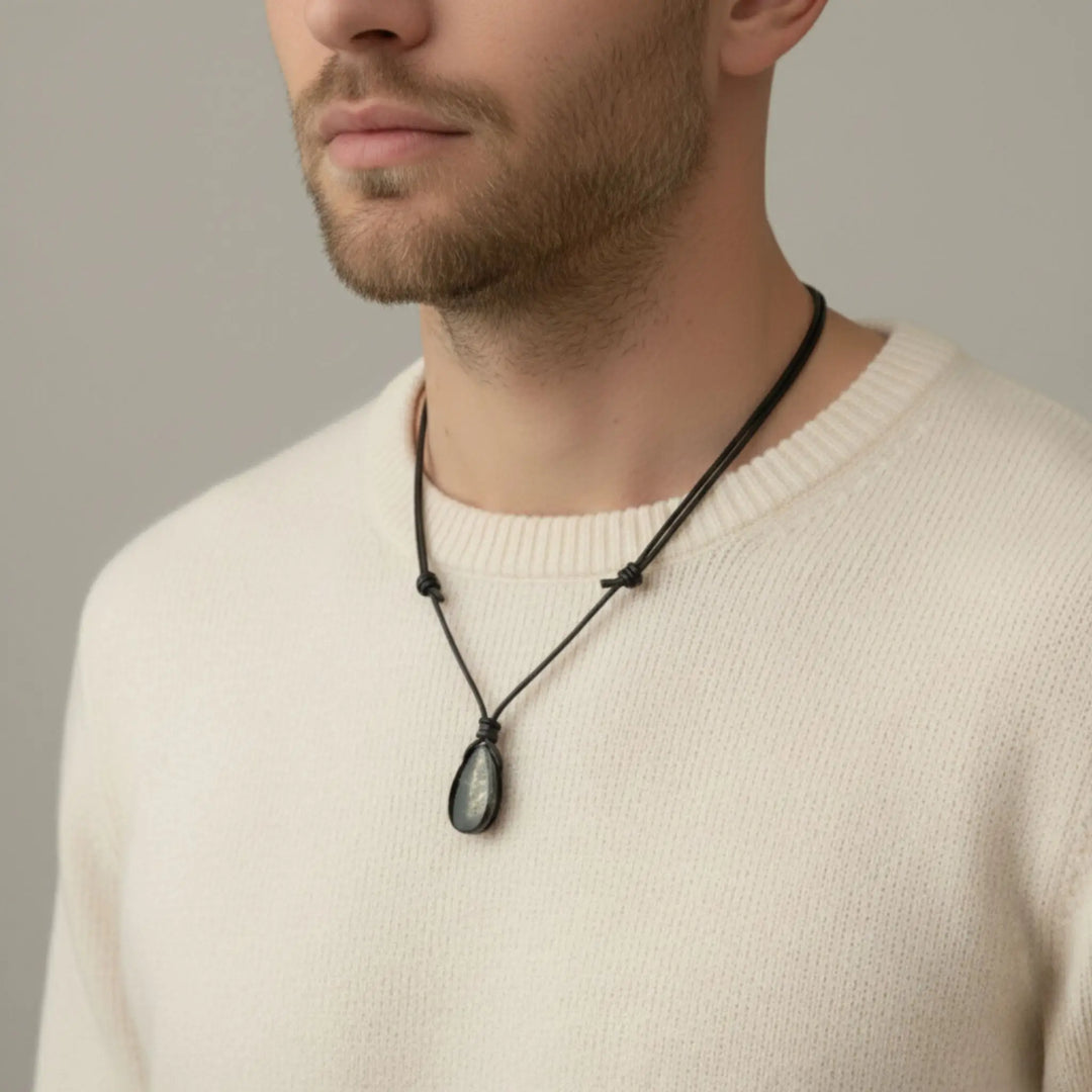 Man wearing a beige sweater with a black nshungite  ecklace against a neutral background