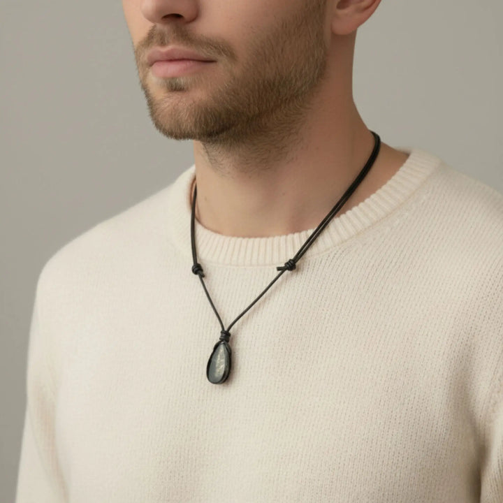 Man wearing a beige sweater with a black nshungite  ecklace against a neutral background