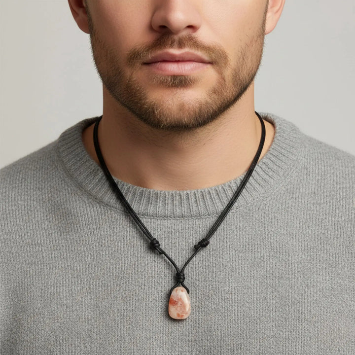 Man wearing a gray sweater with a necklace featuring a sunstone pendant against a neutral background