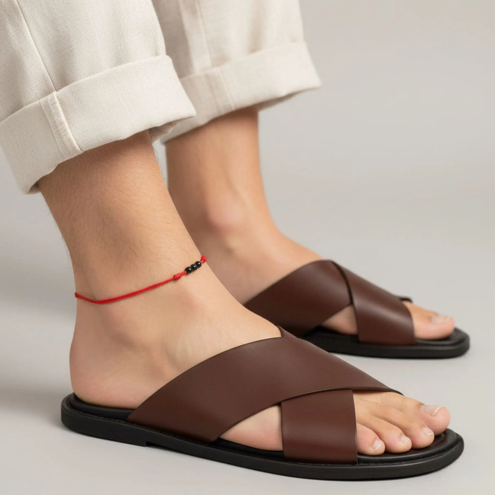 Red string anklet with three natural black tourmaline beads on a men’s ankle, styled brown sandals worn with beige pants on a neutral background