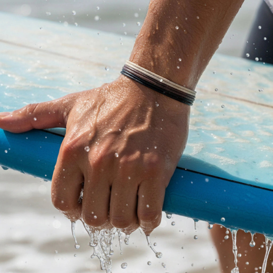 Hand holding a blue hose with water splashing around, wearing stacked bracelets.