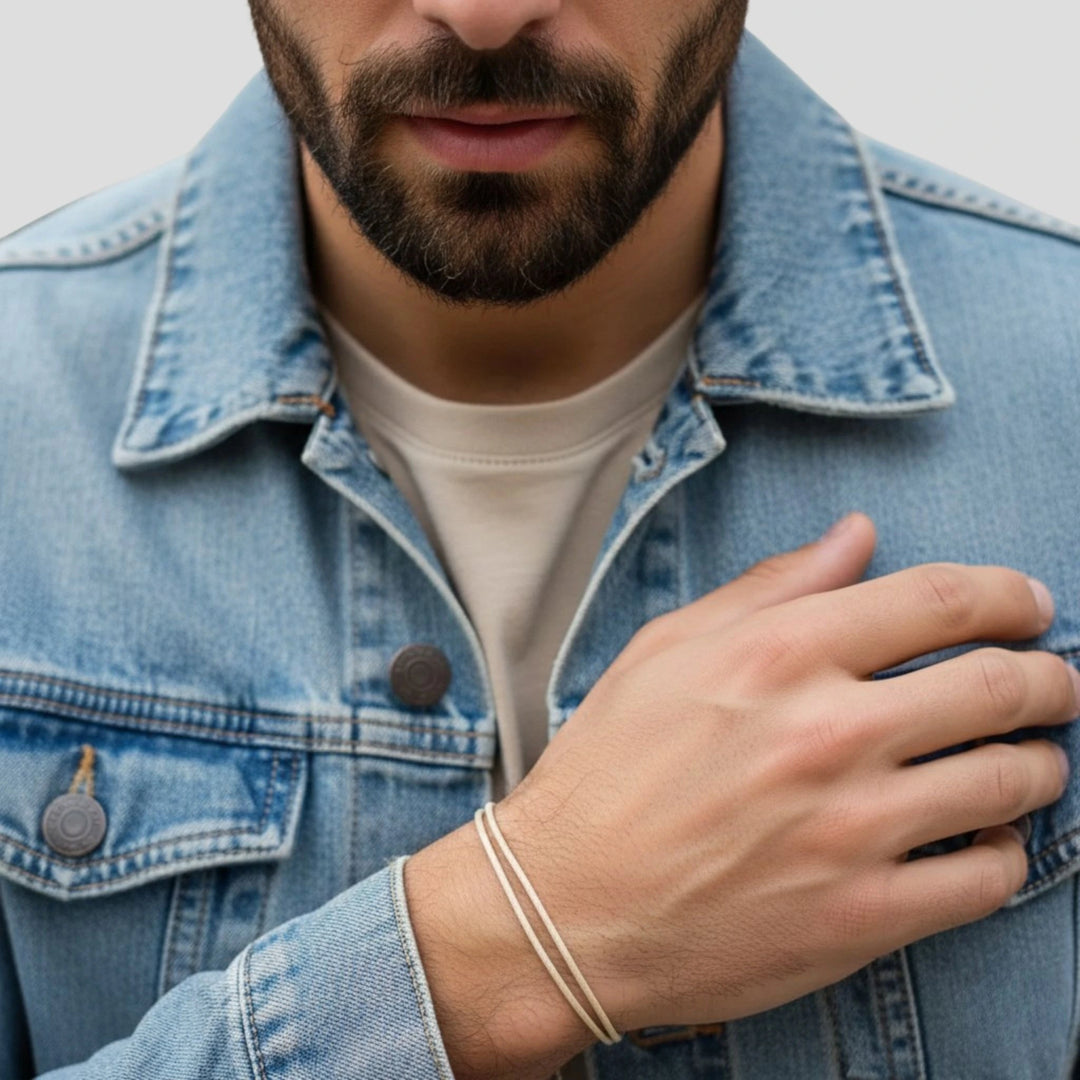 Man wearing a denim jacket with a close-up of his beige cord bracelet. 