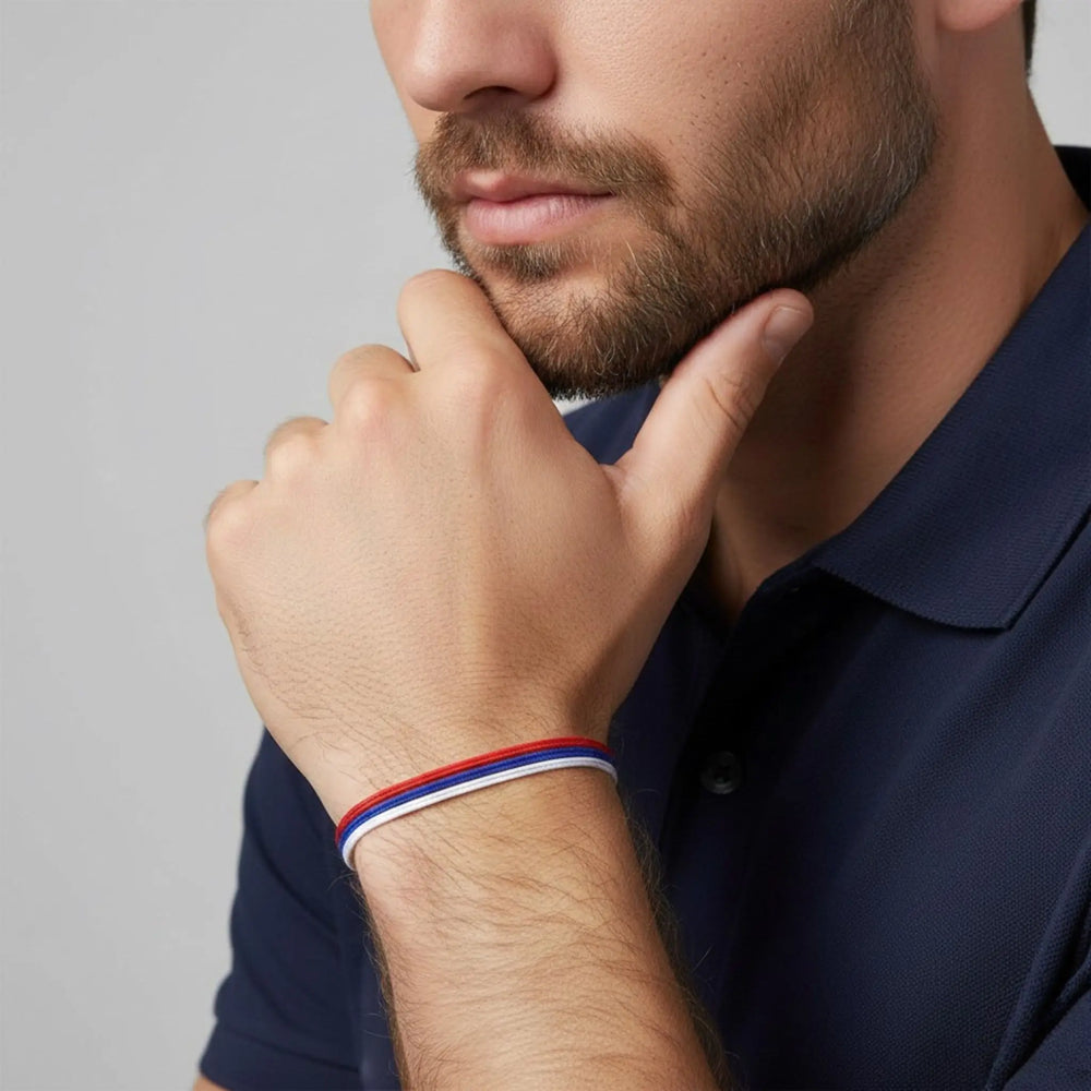 Man wearing a blue shirt with a close-up of his hand and wrist showing a red, white, and blue bracelet.