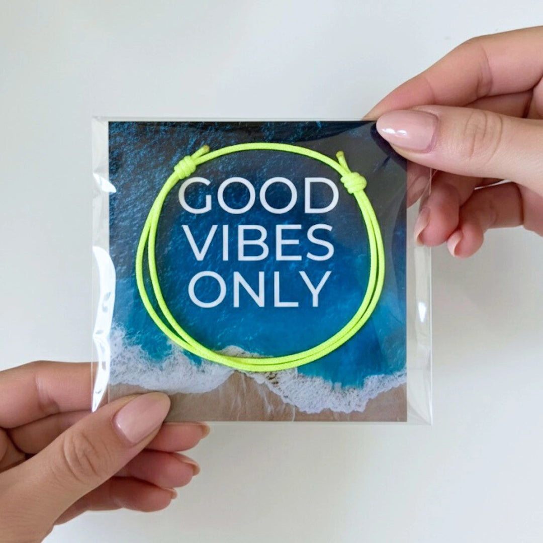 Hand holding a package with a neon yellow bracelet and 'Good Vibes Only' text on a white background