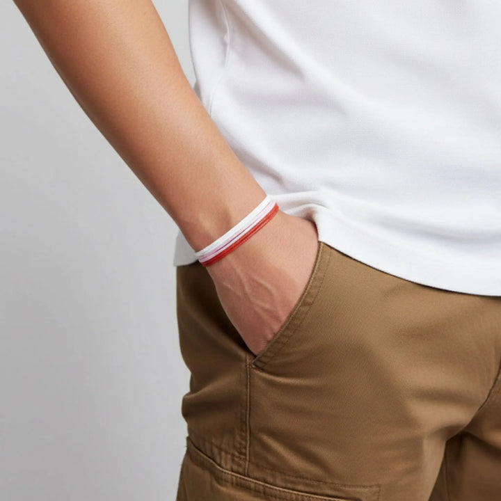 Person wearing a white shirt and brown pants with a red pink and white bracelet on a light gray background