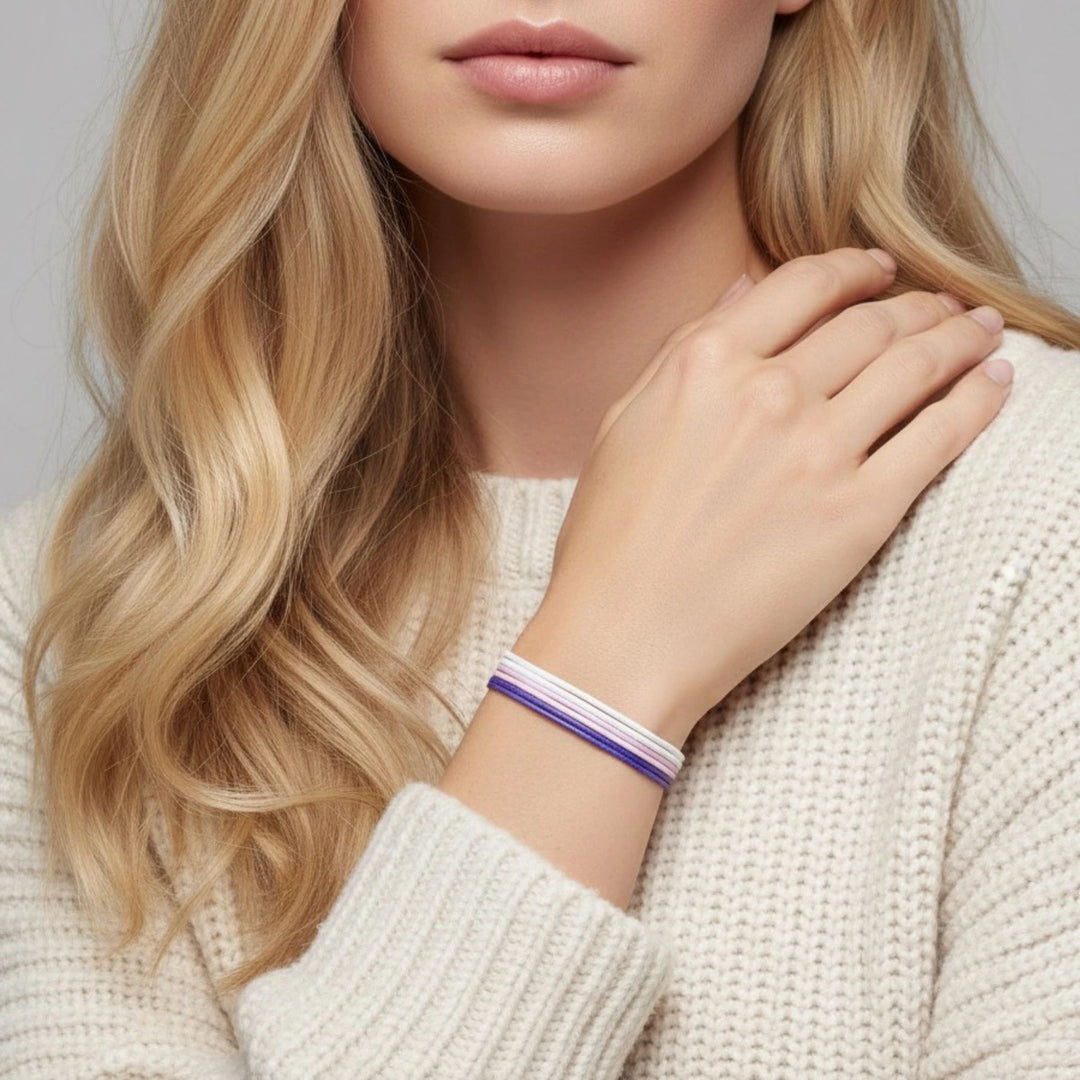 Close-up of a person wearing a purple, pink and white bracelet on a plain background