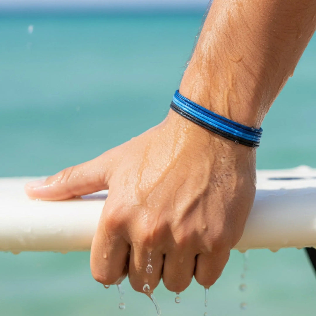 Hand with blue bracelet holding a white surfboard against a blurred beach background