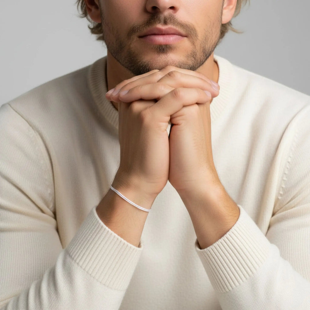 Man wearing a beige sweater with a white bracelet on his wrist, against a neutral background