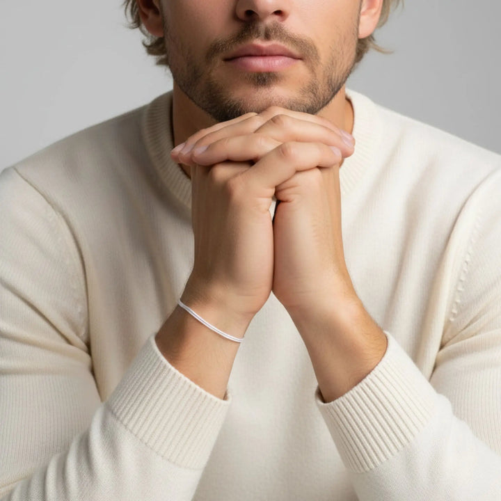 Man wearing a beige sweater with a white bracelet on his wrist, against a neutral background
