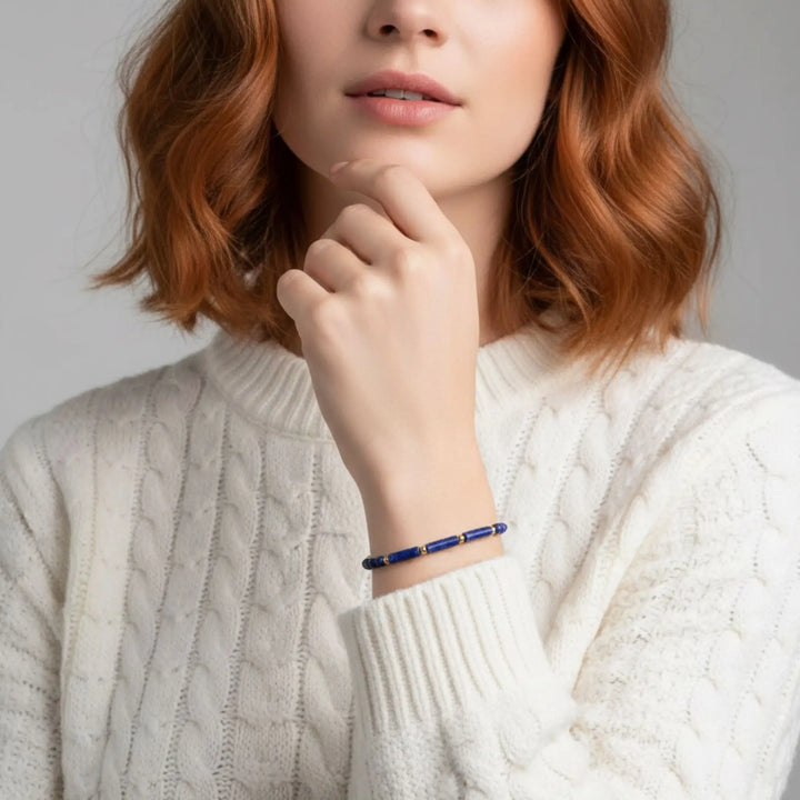 Person wearing a blue lapis lazuli bracelet on his wrist, with a plain background
