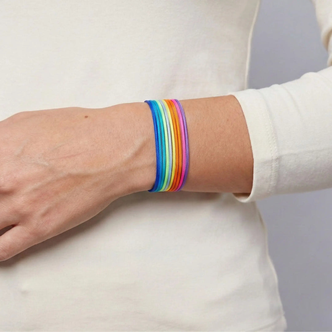 Person wearing a rainbow bracelet on a plain background