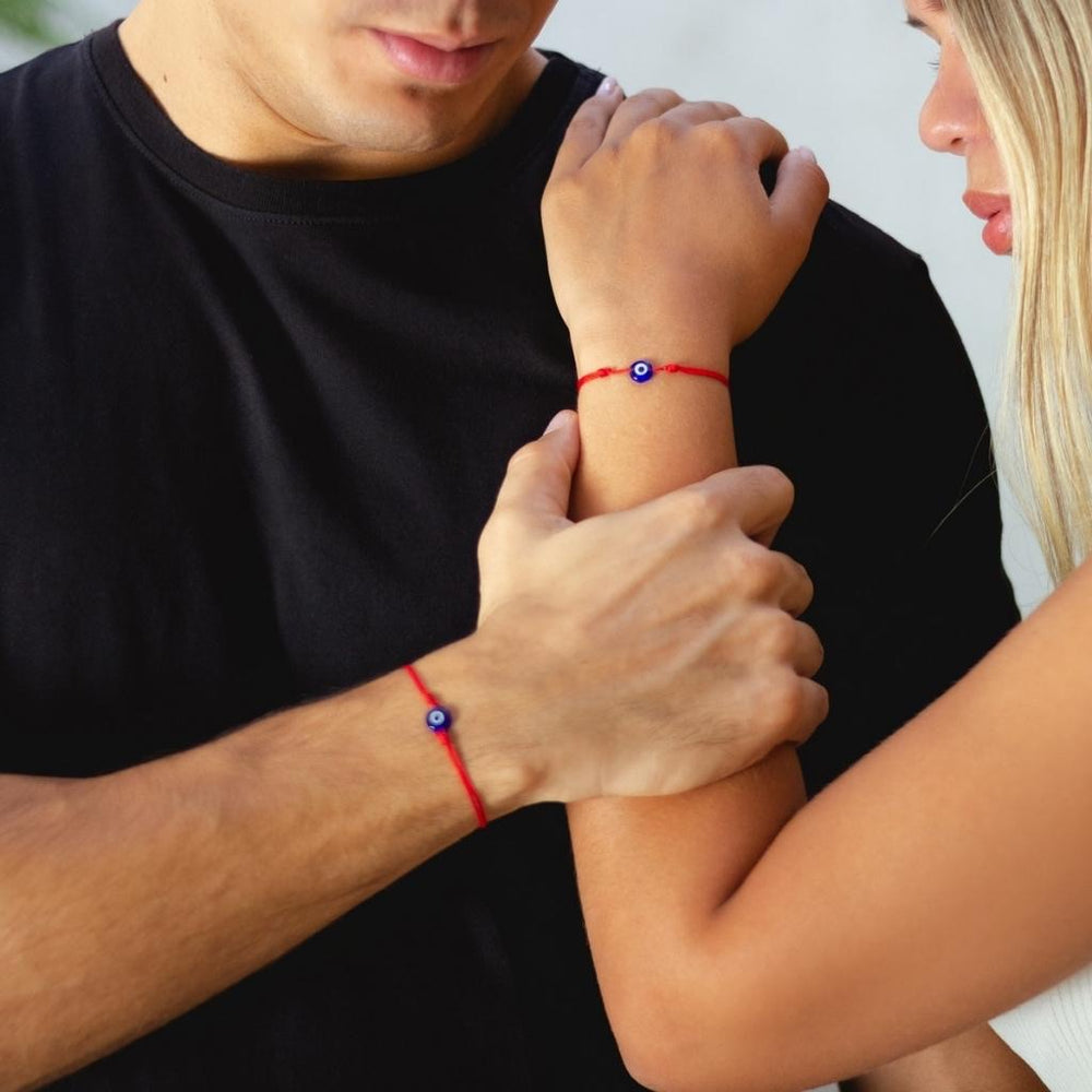 Couple wearing red string bracelets with evil eye charms, symbolizing protection and love - Luck Strings.