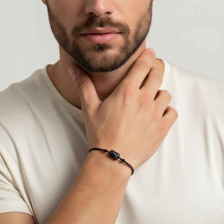 Man wearing raw black tourmaline bracelet on black cord, close-up lifestyle view.
